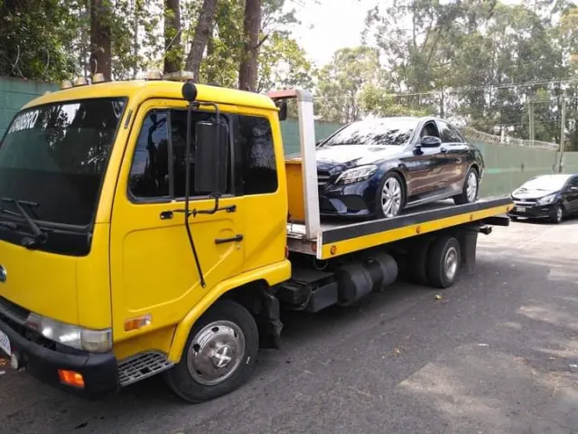 Grúa de plataforma amarilla con un automóvil negro sobre la plataforma