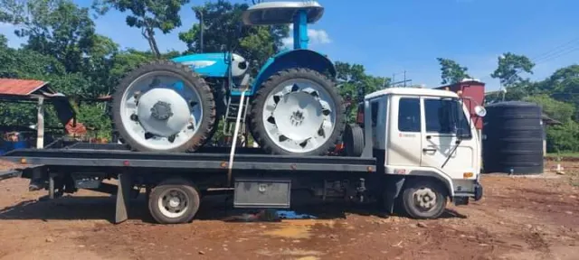Camión de plataforma transportando un tractor azul